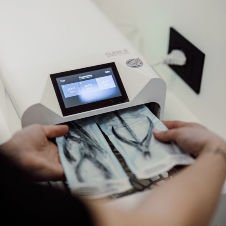 Staff member loading sealed instrument pouches into a Class B autoclave for sterilisation.